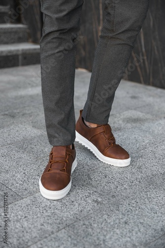 Close-up photo of men's legs with leather brown sneakers. Genuine leather shoes with white soles. Sneakers for businessmen. © Alex