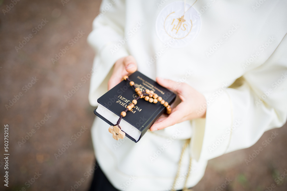 Dziecko przystępujące do sakramentu Pierwszej Komunii Świętej trzyma w ręku różaniec i modlitewnik - obrazy, fototapety, plakaty 