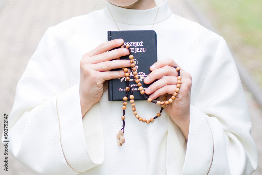 Dziecko przystępujące do sakramentu Pierwszej Komunii Świętej trzyma w ręku różaniec i modlitewnik - obrazy, fototapety, plakaty 