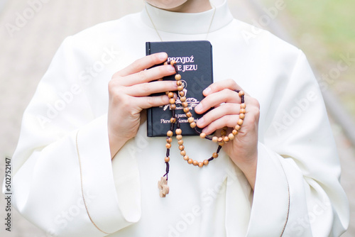Dziecko przystępujące do sakramentu Pierwszej Komunii Świętej trzyma w ręku różaniec i modlitewnik