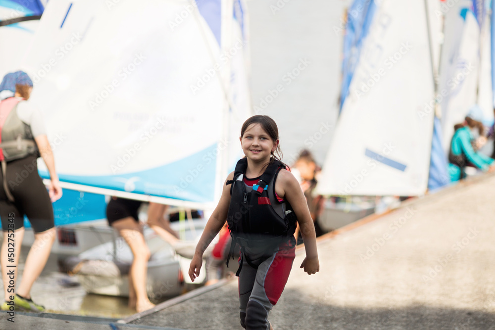 Mała żeglarka szykuje swoją łódkę klasy optymist do pływania po jeziorze - obrazy, fototapety, plakaty 
