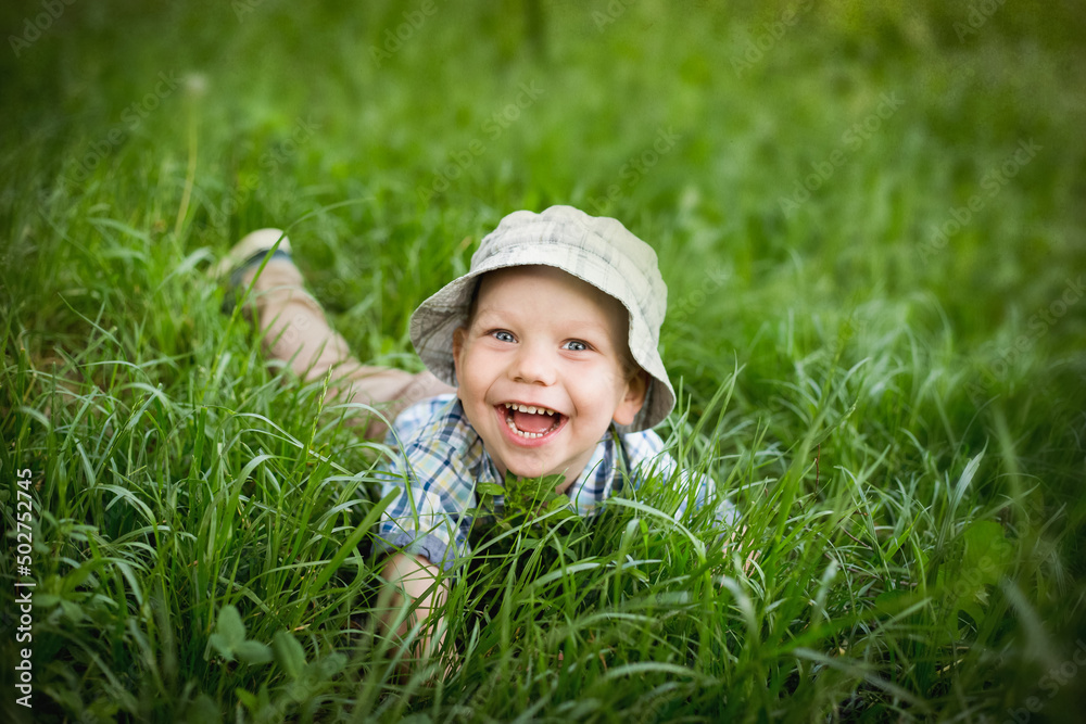 Chłopiec tarza się w trawie i śmieje w głos, dziecko turla się i leży na trawie z radością - obrazy, fototapety, plakaty 