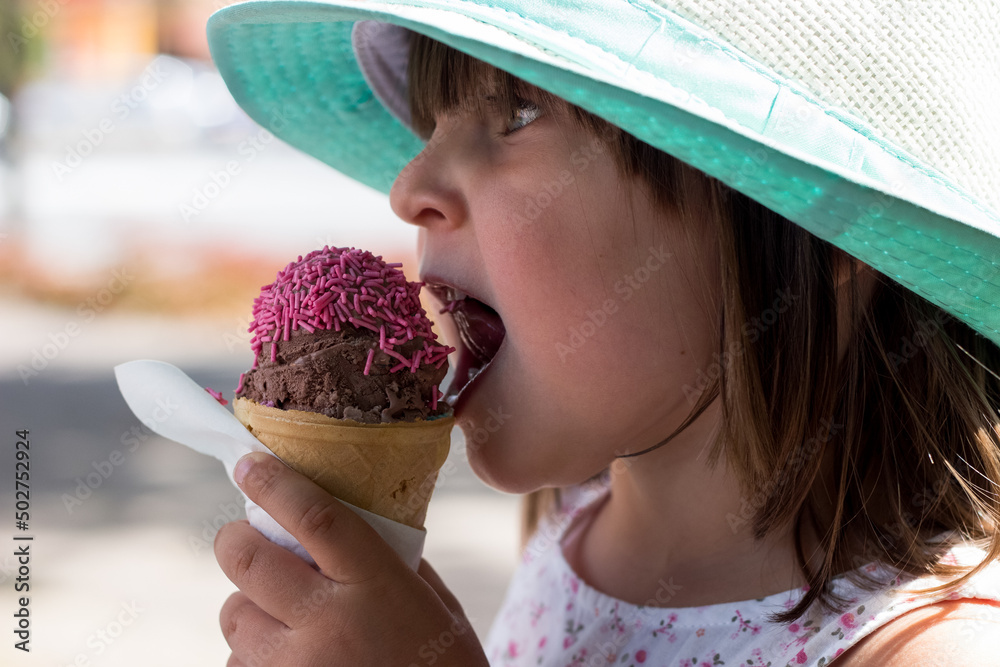 Mała dziewczynka w kapeluszu je lody truskawkowe, wakacyjna ochłoda, dzieci lubią lody - obrazy, fototapety, plakaty 