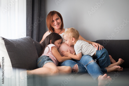 Kobieta w ciąży ze swoimi dziećmi siedzi w domu na kanapie, mama przytula w objęciach swoje dzieci
