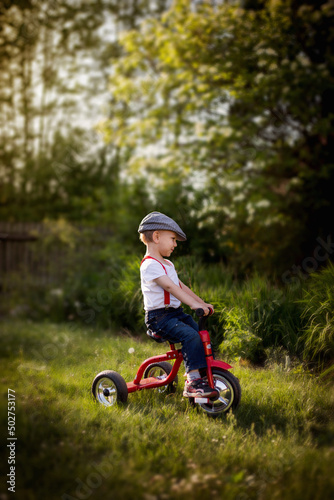 Chłopiec uczy się jeździć na rowerze trójkołowym w letnim słońcu © Katarzyna Krociel
