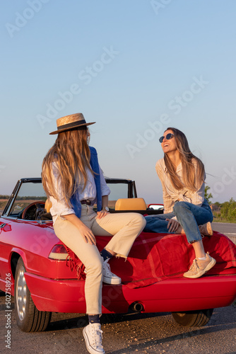 Happy female friends cheering sitting in a convertible red carat sunset time with golden light and light flare © NOWRA photography