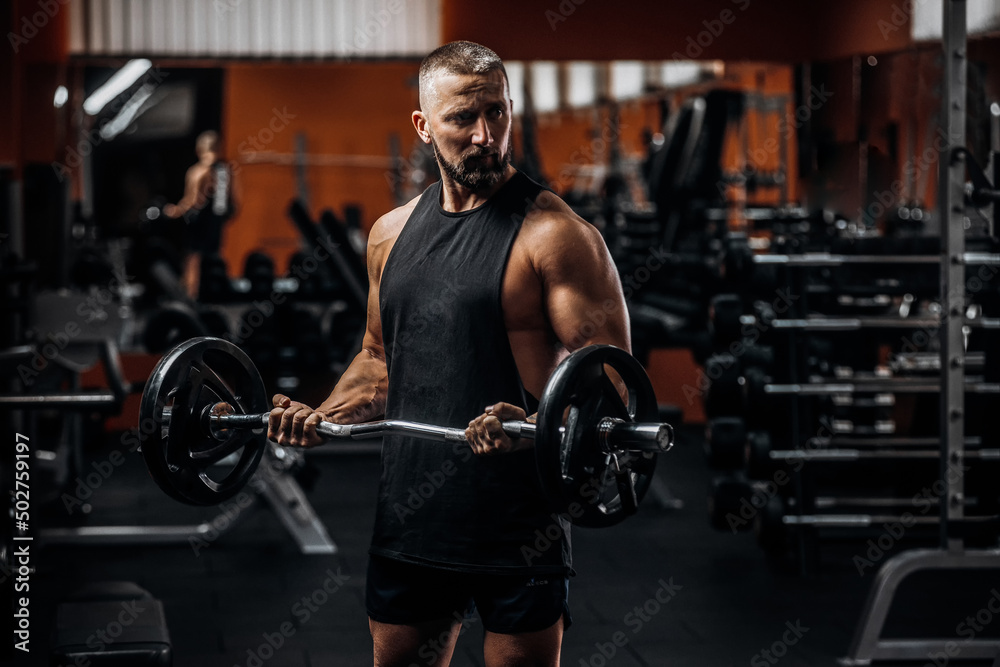 Fit strong man doing biceps curl with barbell in gym Fit strong man doing biceps curl with barbell in gym