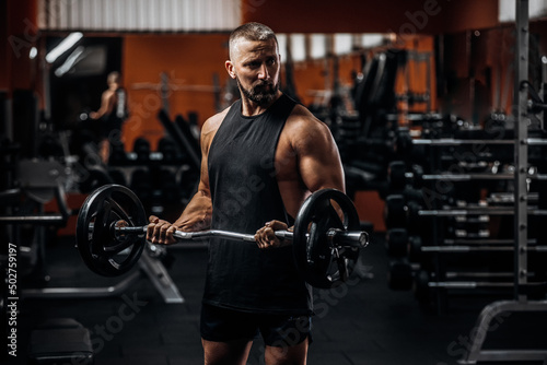 Fit strong man doing biceps curl with barbell in gym photo