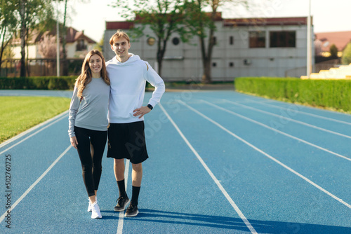 Athletic smiling couple wearing sportswear posing in the stadium. Guy and girl looking at the camera. A place for your text