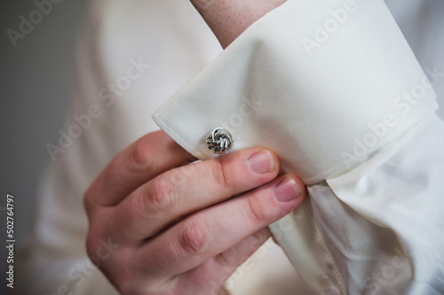Bild auf Leinwand Elegant close-up of a man adjusting a silver knot cufflink on a white dress shirt cuff