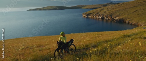 The girl towing gravel bike at picturesque sunset. The woman travels on a bicycle with bikepacking green color bags in modern style. Live handheld camera.