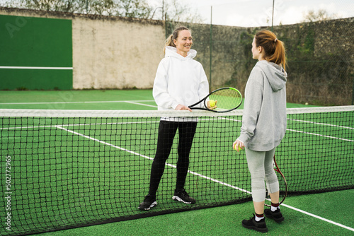 Happy caucasian mother and daughter playing tennis on tennis court outdoors