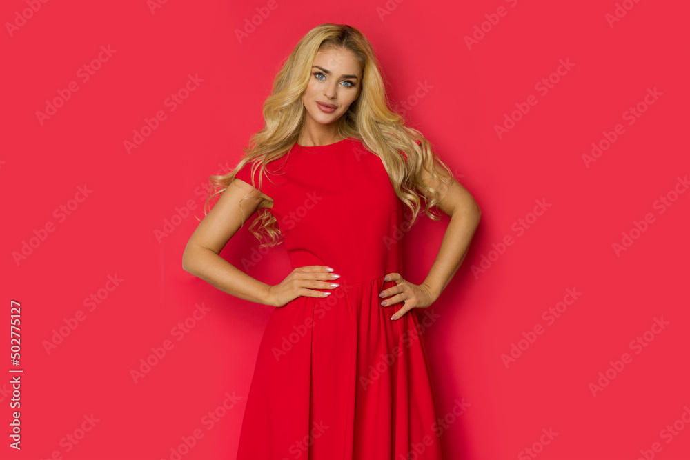 Beaitufl blond woman in red dress is posing with hands on hip