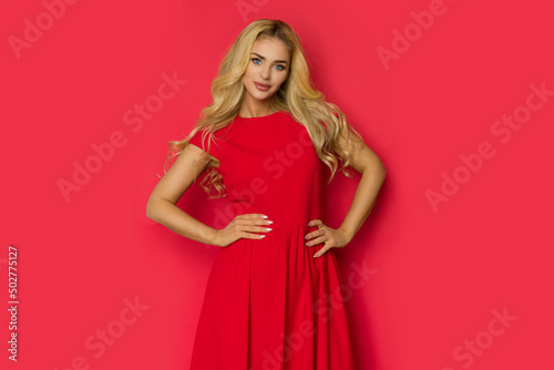 Beaitufl blond woman in red dress is posing with hands on hip
