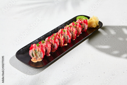 Modern asian food - maki with tobiko on black plate on white concrete background. Sushi roll with tobiko caviar and spicy sauce outside. Maki sushi with masago caviar and spicy mayo top.