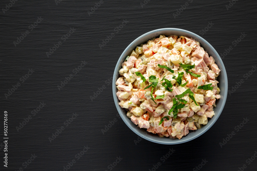 Homemade Olivier salad in a Bowl on a black wooden surface, top view. Flat lay, overhead, from above. Space for text. Homemade Olivier salad in a Bowl on a black wooden surface, top view. Flat lay, overhead, from above. Space for text.