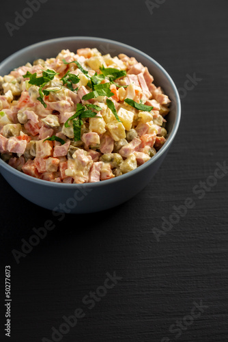 Homemade Olivier salad in a Bowl on a black wooden background, side view. Copy space.