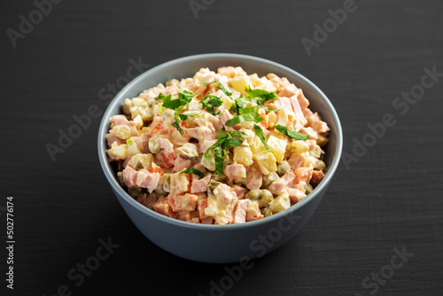 Homemade Olivier salad in a Bowl on a black wooden surface, side view.