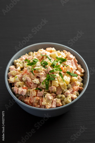 Homemade Olivier salad in a Bowl on a black wooden background, side view.
