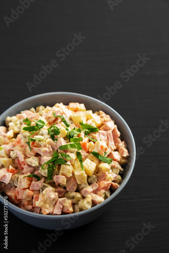 Homemade Olivier salad in a Bowl on a black wooden background, low angle view.