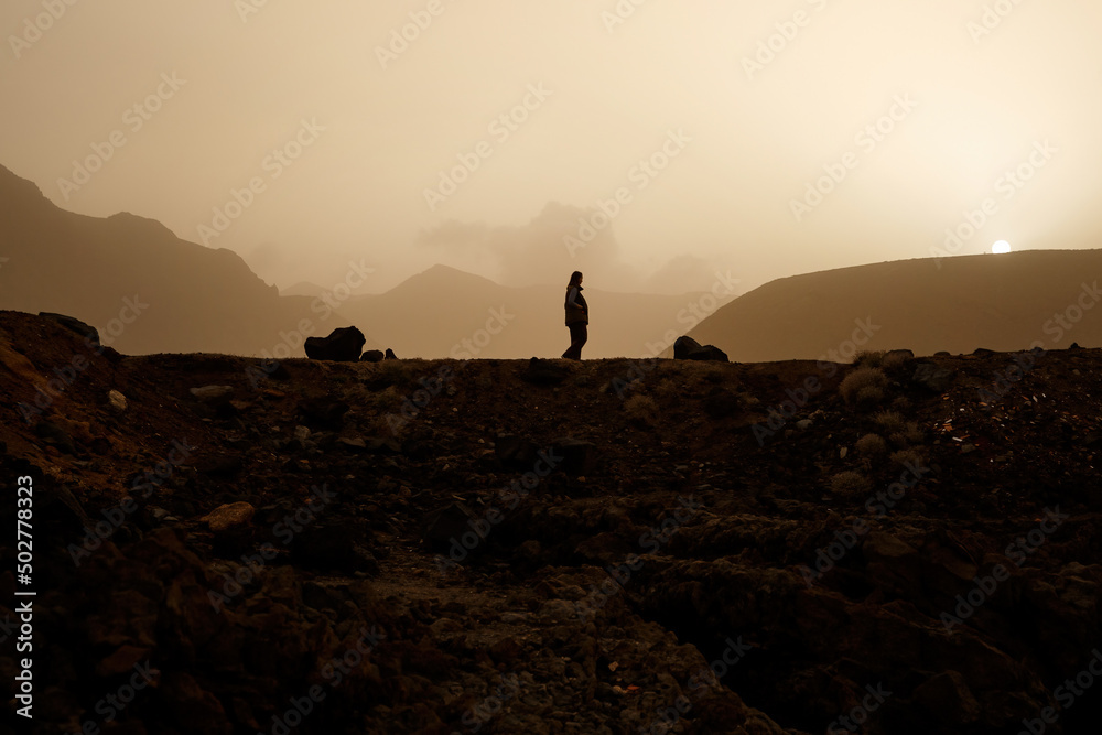 The woman is walking in the volcano park desert during smoky sunset