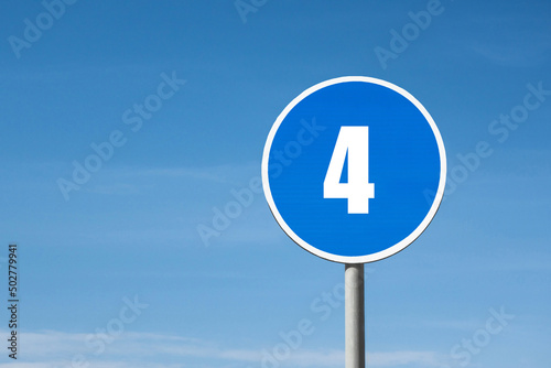 '4 (four)' sign in blue round frame. Blue sky is on background