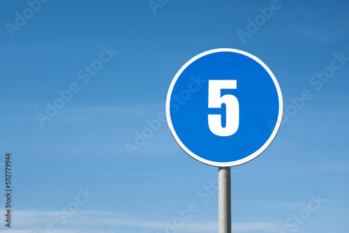 '5 (five)' sign in blue round frame. Blue sky is on background
