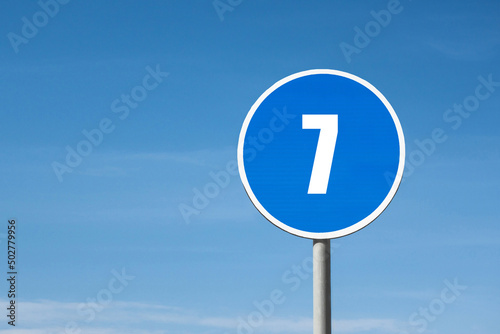 '7 (seven)' sign in blue round frame. Clear sky is on background