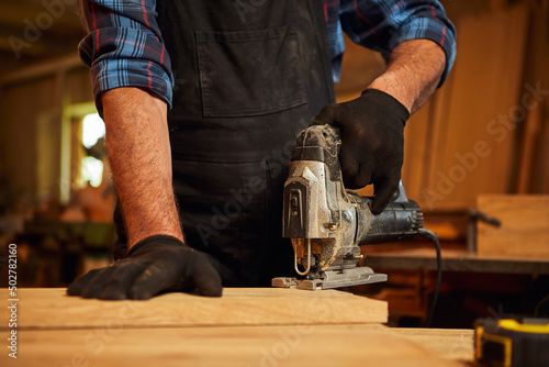 Close up of professional carpenter hands sawing wood with an electric jigsaw in the carpentry workshop