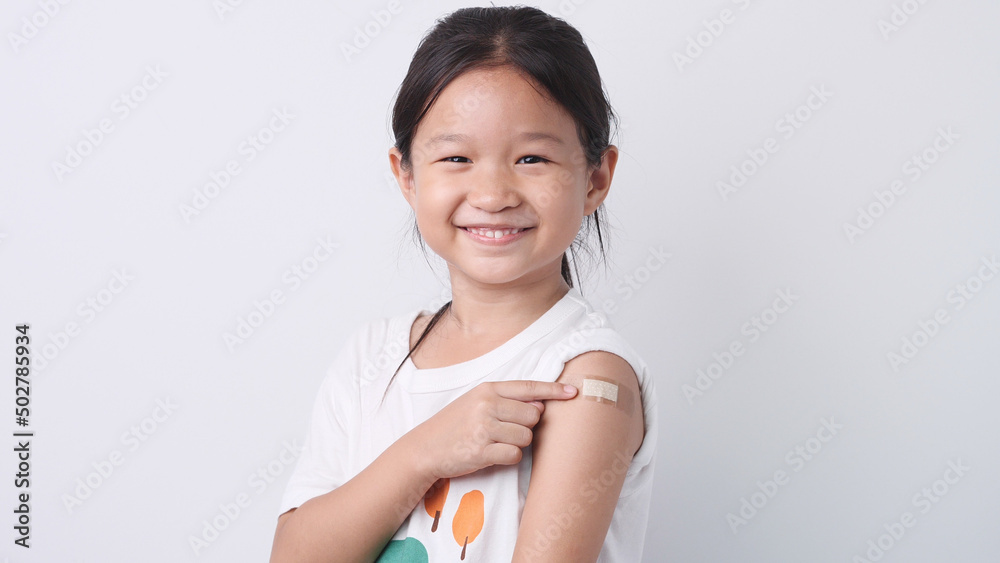 Vaccine concept. Happy Asian little child girl smiling, showing arm with plaster bandage after received, getting COVID-19 vaccine injection. Concept of inoculation, vaccinate, campaign, COVID19, Flu - obrazy, fototapety, plakaty 