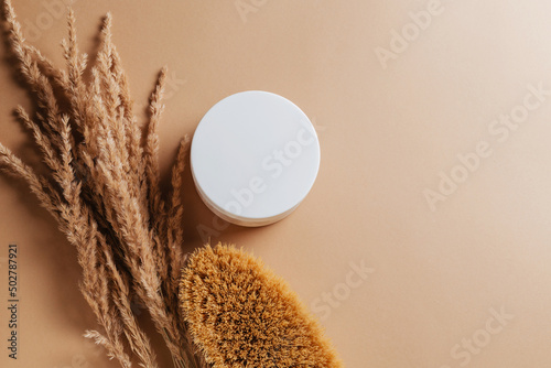 Natural massage brush with a jar of scrub and dried flowers on a brown background. Stylish concept of massage, cosme tics and flatlay body care photo