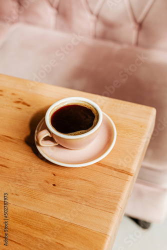 Black strong coffee in a pink ceramic cup on a wooden table. Aromatic freshly brewed Americano for breakfast