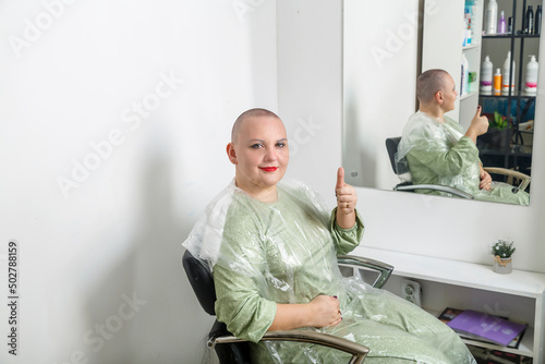 Smiling shaved bald woman with bright make-up in the hairdresser's chair.