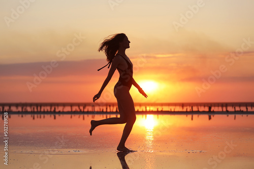 silhouette of a young slim woman in a swimsuit who dancing at sunset on the sea. summer holiday