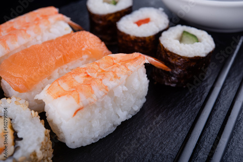 Close up of delicious japanese food with sushi rolls  with salmon, tuna,   shrimp with black chopsticks  on black background