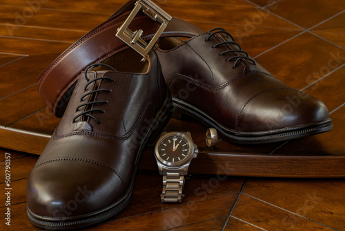 Accessories for wedding groom of shoes, belt, watch, and ring on a shiny wooden surface