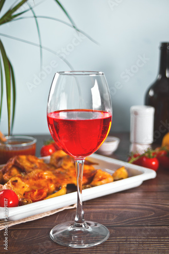 Glass of red wine and food chicken tabaka with vegetables on the baking sheet on the background.