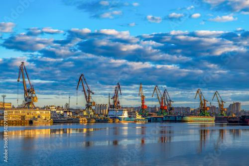 Ships, barges in soft focus in the cargo port against the background of sunset, dawn, in the rays of the sun in Cherepovets, Russia. Industrial urban landscape, transport logistics.