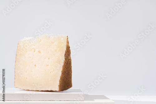 Trozo de queso manchego de oveja curado sobre una mesa blanca. Aperitivo español	 photo