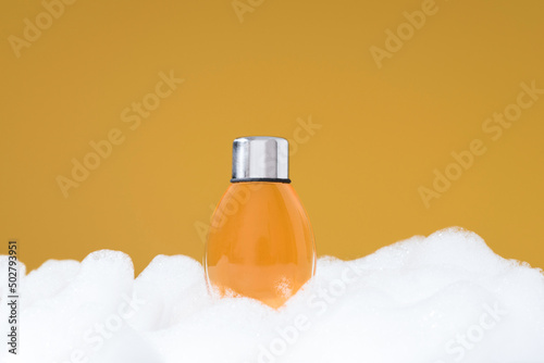 Botella de gel de ducha sobre espuma. Jabón de baño para el cuidado de la piel sobre fondo naranja	 photo