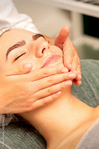 Beautiful caucasian young woman receiving a facial massage with closed eyes in spa salon  close up. Relaxing treatment concept