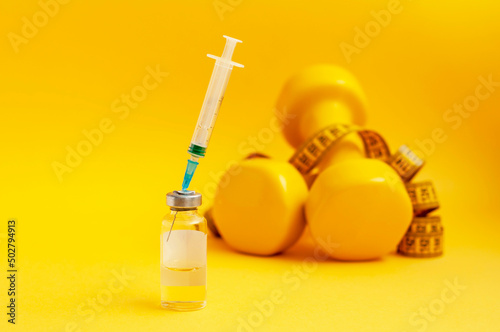 syringe is stuck in jar, dumbbells and a measuring tape are lying next to it on a yellow background, close-up. the concept of doping in sports, steroids, testosterone and other drugs for weight loss.