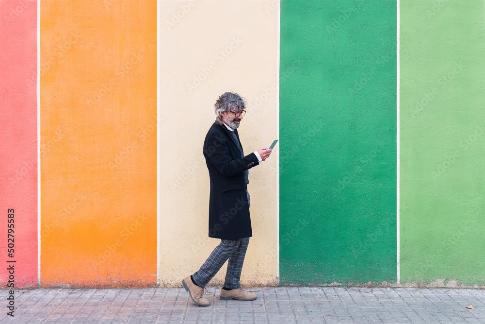 Mature businessman using mobile phone near color palette wall. Colorful background Mature businessman using mobile phone near color palette wall. Colorful background