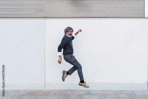 Mature man looking at camera while jumping on footpath