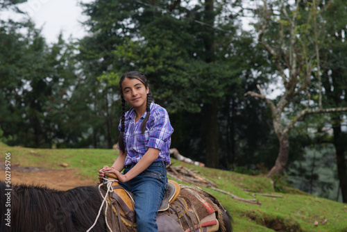 Portrait of a girl riding a horse smiling at the camera in the forest.