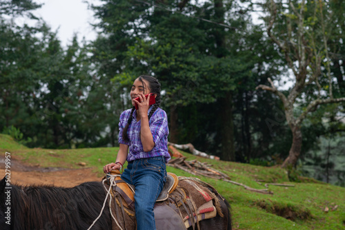 A girl talks on the phone while riding her horse.