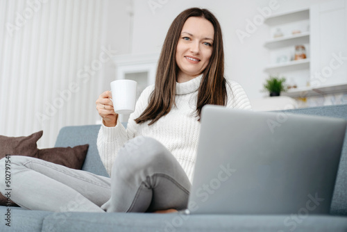 young woman sitting on the couch and using a laptop .