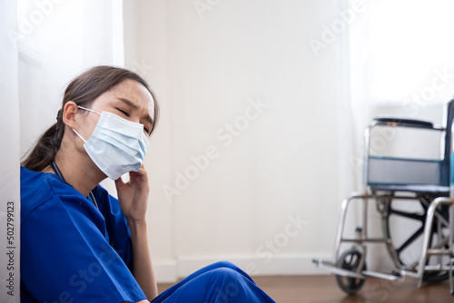 Beautiful nurse wears surgical mask after caring for a bedridden patient. She got tired after a hard day's work and collapsed on the wall near the curtains. photo