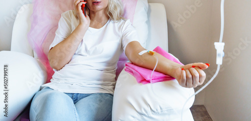 Woman in hospital talking at mobile phone while needle is in arm, Vitamin Therapy Iv Drip Infusion In Women Blood photo