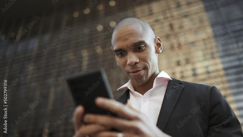 Pretty African businessman texting by mobile on the street Pretty African businessman texting by mobile on the street
